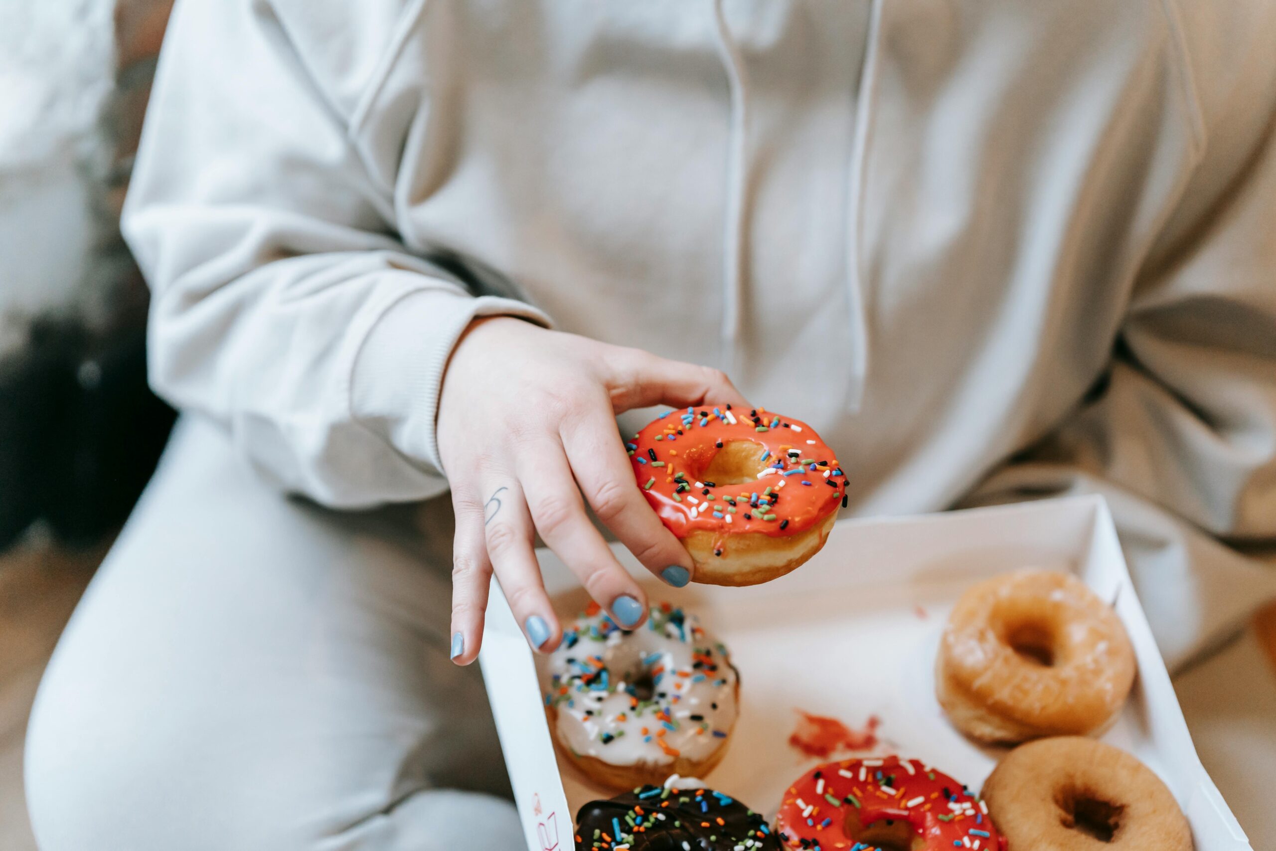 A person holding a colorful sprinkled donut, highlighting the theme of sugar addiction as discussed in the blog post.